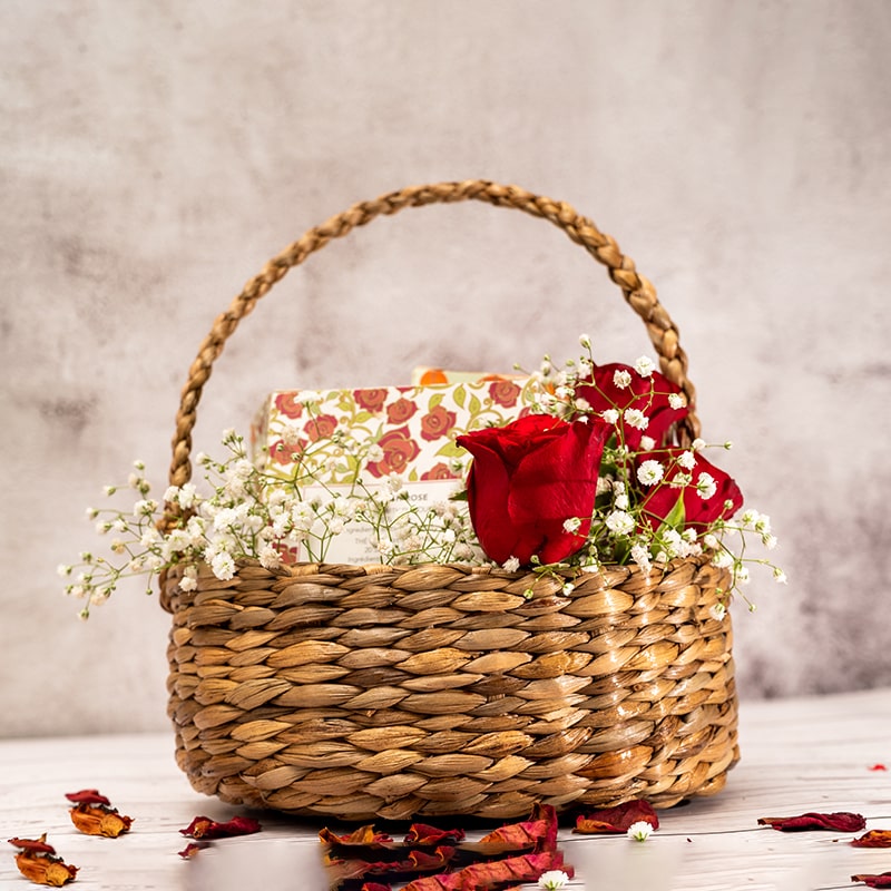 A close-up view of a handwoven wicker basket with a natural brown color and a sturdy, structured shape. The basket features a tightly woven pattern with small gaps between each piece of wicker, and two handles on either side for easy carrying. The wicker material gives the basket a rustic, earthy feel, making it a versatile and stylish storage solution for a variety of items