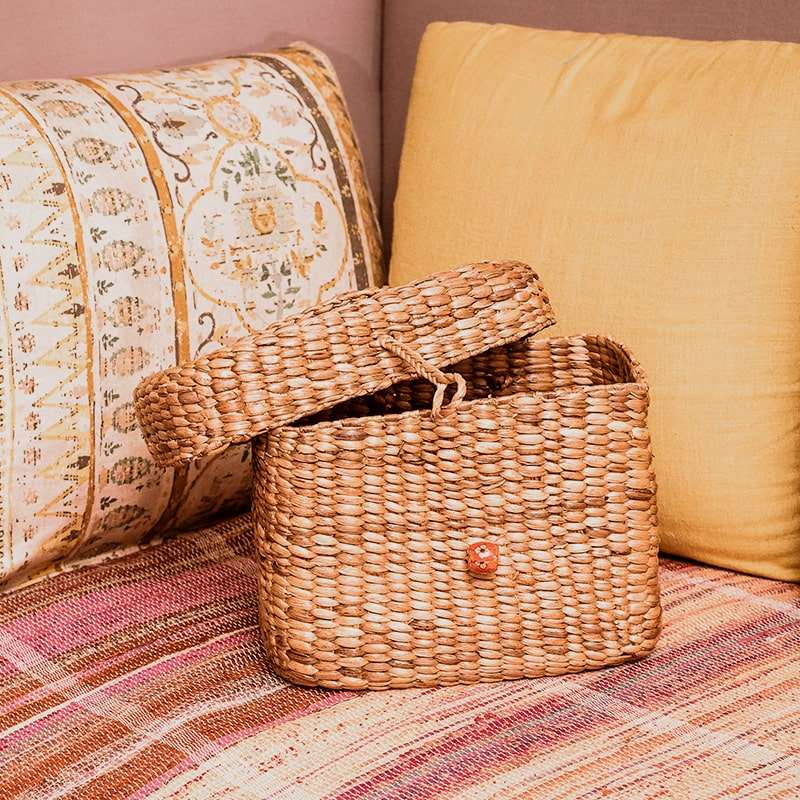 An oval-shaped wicker basket with a hooded top. The basket is made of woven light-brown wicker and has a handle on top for easy carrying. The hooded top is also made of wicker and can be opened to reveal the inside of the basket